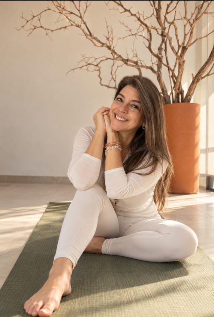Inicio — Nueva propuesta para revisión Loretta sentada en su mat de Yoga, sonriendo.